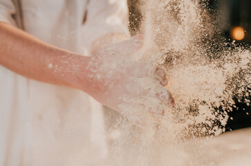 Fototapeta premium Hand smashes through white powder, creating a dynamic explosion. Dust particles float in warm, golden light. The motion suggests energy, creativity, or celebration