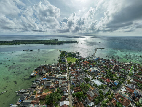 Aerial view of the town extending into the turquoise sea, the vibrant greens of the island contrasting with the white clouds, Karimunjawa, Central Java, Indonesia.