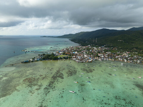 Aerial view of the vibrant Karimunjawa Town Square nestled between the turquoise sea and verdant hills, Karimunjawa, Central Java, Indonesia.