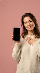 Fototapeta premium Smiling Woman Presenting Blank Smartphone Against Pink Background