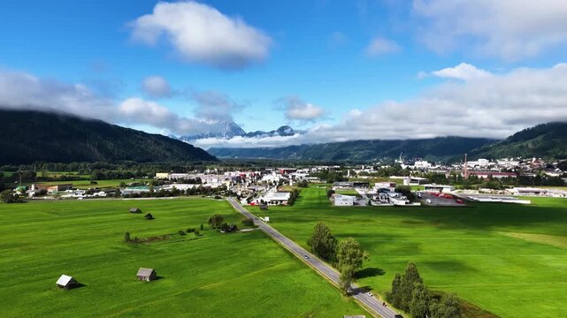 Cinematic aerial drone shot of green fields and road leading toward the city of Innsbruck with the dramatic Serles mountain peak in the background in Tyrol, Austria.