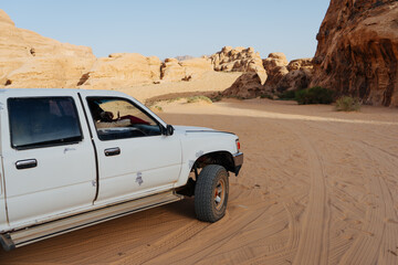 Obraz premium Wadi Rum, Jordan, 12.2.2026: Off-road pickup truck driving through the desert landscape of Wadi Rum in Jordan. Scenic view of a 4x4 vehicle exploring sandy tracks between sandstone rock formations in 