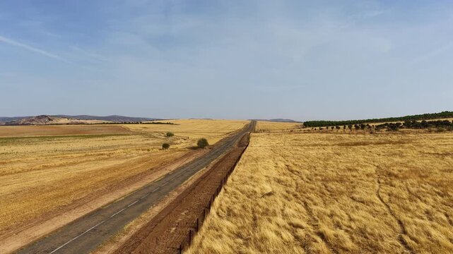 Aerial drone flight above a long empty road crossing dry agricultural fields in the La Mancha plains near Consuegra in the region of Castilla-La Mancha. Scenic Spanish countryside landscape often asso
