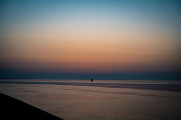 Obraz premium A peaceful sunrise over the tranquil Wadden Sea with soft colors, a view of the North Sea or the Jade Bay in the morning at the lock island in 26382 Wilhelmshaven, Germany.