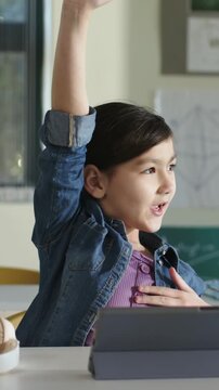 Vertical video: Raising arm after cue student in jean jacket with hand on chest at desk with tablet