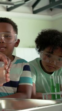 Vertical video: Spotting green tubes, striped teen pouring into tray in lab, goggles on observing