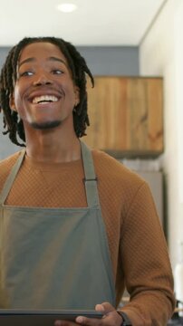 Vertical video: Reading phone, gray-aproned barista looking up to greet at counter holding tablet