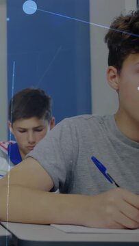 Vertical video: Camera shifting close to teen boy writing with blue pen, concentrating on classwork