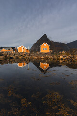 Obraz premium Stunning fall scenery in the Lofoten Islands. Iconic red rorbu cabins nestled between rocky coastlines and dark arctic waters during the golden hour. Travel Norway.
