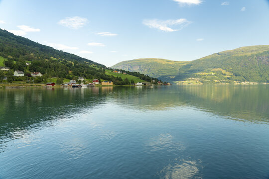 View of the serene lake reflects the lush green mountains under a vast blue sky, dotted with fluffy white clouds, Olden, Vestland, Norway.