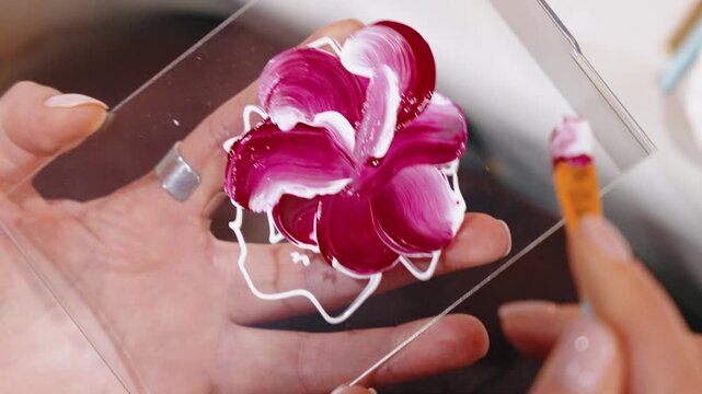 Artist painting a pink flower on glass. Creative artist holding a glass pane while painting a beautiful pink flower with acrylics