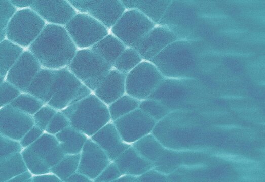 Abstract turquoise water caustics and ripple pattern on pool floor