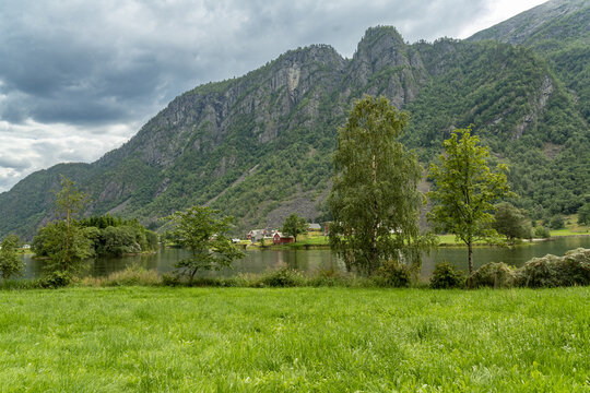 View of lush green meadow leading to the tranquil lake mirroring verdant mountains under a moody sky, Sandvinvatnet, Odda, Vestland, Norway.