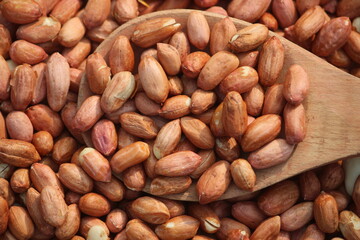 red peeled peanuts in wooden spoon texture background.	