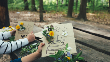 Children creating nature art with flowers and drawings on cardboard outdoors © shine.graphics