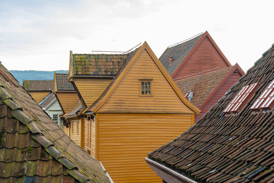 View of vibrant wooden buildings with striking triangular roofs cascade in a warm, inviting scene, Bryggen, Bergen, Norway.