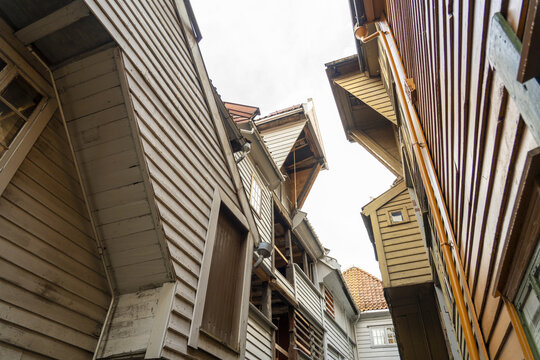 View of aged wooden buildings angled towards each other in a narrow street on a cloudy day, creating a unique architectural perspective, Bergen, Norway.