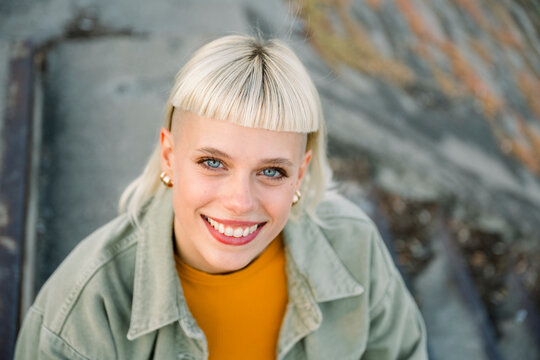 Smiling woman with blonde hair and short bangs sitting outdoors