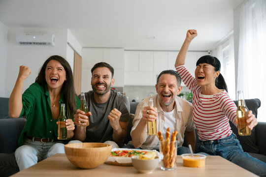 Friends celebrating football match at home with drinks and snacks