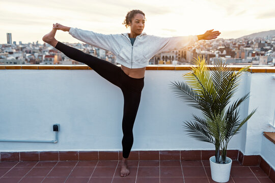 Woman balancing in yoga pose on rooftop terrace at sunrise overlooking city
