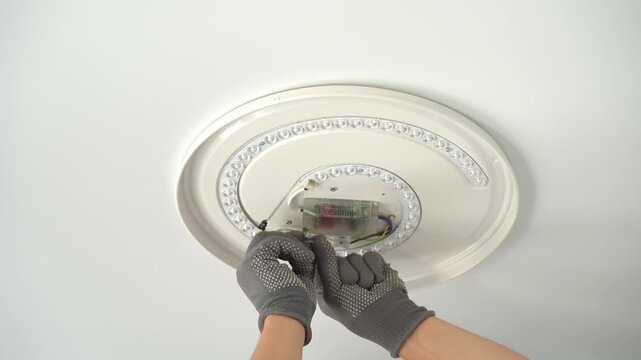 Close up of electricians hands installs ceiling LED lamp on suspended ceiling at home. Hands connect wires of lamp frame. Installation light