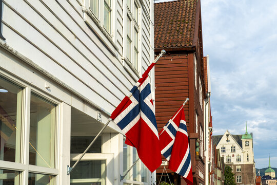 View of vibrant Norwegian flags fluttering proudly against the backdrop of white and red wooden buildings, Bergen's architectural charm, Bergen, Vestland, Norway.