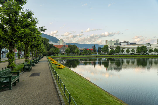 View of tranquil Lille Lundgegardsvannet mirror the cityscape, bordered by verdant lawns and shaded benches, inviting serenity and reflection, Bergen, Vestland, Norway.