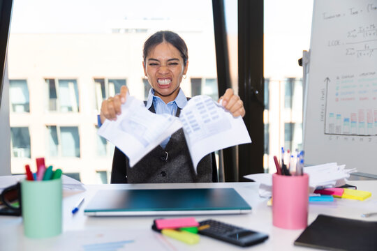 Employee angrily tearing documents at office desk in corporate workplace