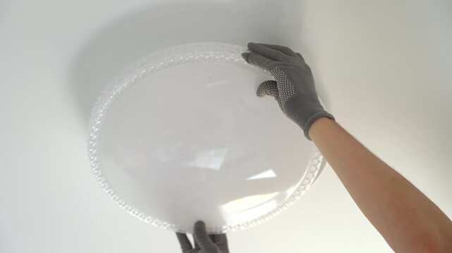 Close up of electricians hands installs ceiling LED lamp on suspended ceiling at home. Hands connect and fix lampshade. Installation light