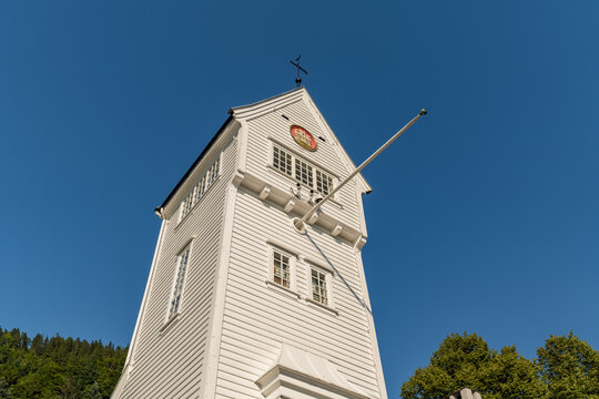 View of a striking white wooden tower with a cross atop its peak under a clear blue sky, standing tall in the sunlight, Bergen, Vestland, Norway.