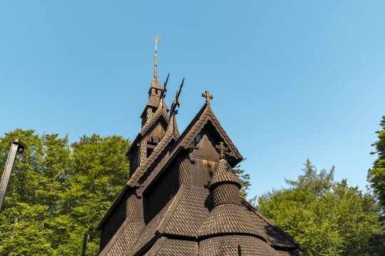 View of majestic Fantoft stave church, its dark wood contrasting against the vibrant green foliage and the clear blue sky, Bergen, Vestland, Norway.
