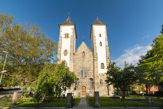View of the imposing stone facade of St. Mary's Church rises beneath a crisp blue sky, framed by lush greenery, Bergen, Vestland, Norway.