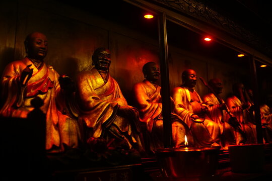 Row of golden monk statues illuminated by warm light inside Kelenteng Eng An Kiong temple, Malang, East Java.