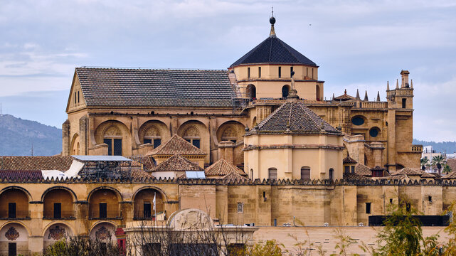 View of the Mezquita-Cathedral's striking domes and arches rise in warm hues against a cloudy sky, a testament to centuries of rich history, Cordoba, Andalusia, Spain.
