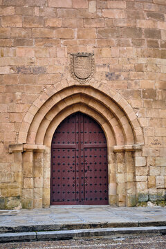 View of an ancient stone facade with a grand arched doorway featuring a dark wooden door studded with metal, Salamanca, Castile and Leon, Spain.