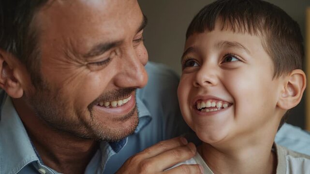 Leaning father in light-blue shirt making son in light tee laugh at home, hand-on-shoulder bonding