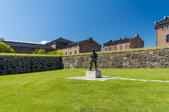 View of Max Manus bronze statue stands proudly on a stone plinth amidst a vibrant green lawn, by a stone wall in Akerhus fortress, Oslo, Oslo, Norway.