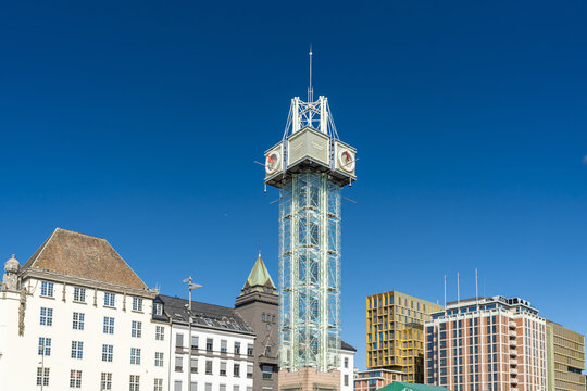 View of a modern clock tower rising above historic buildings under a clear blue sky on a sunny day, Oslo, Oslo, Norway.