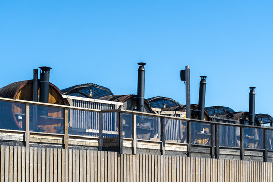 View of a row of wooden barrel saunas with black chimneys puncturing the bright blue sky above a wooden fence, Oslo, Oslo, Norway.
