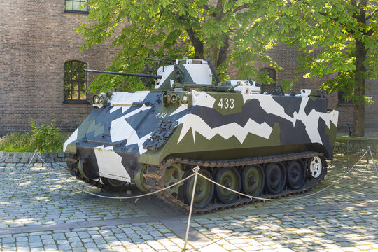 View of a military tank with a camouflage pattern sits prominently on a cobblestone surface near an old brick building, Oslo, Oslo, Norway.