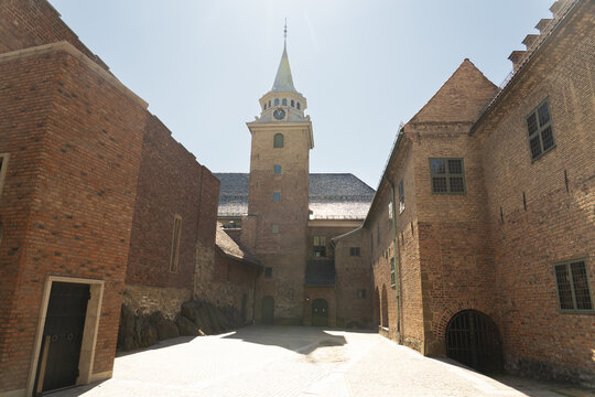 View of medieval brick buildings and a clock tower bathed in sunlight, framing a journey through time and architectural wonder, Oslo, Oslo, Norway.
