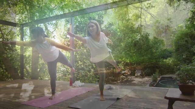 Animation of happy asian mother and daughter practicing yoga over trees