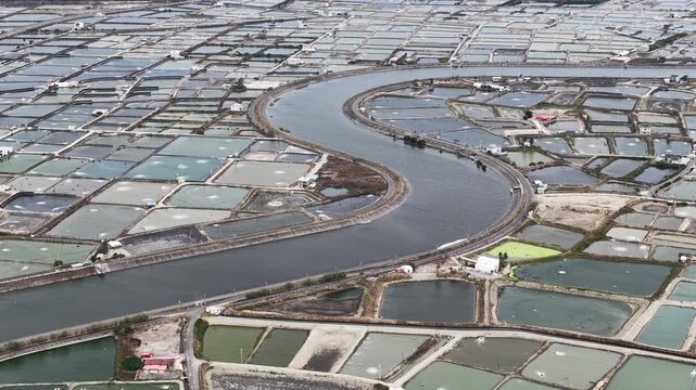 High altitude aerial view showing the geometric patterns of aquaculture ponds and shrimp farms divided by a winding s shaped river, revealing a vast man made agricultural landscape
