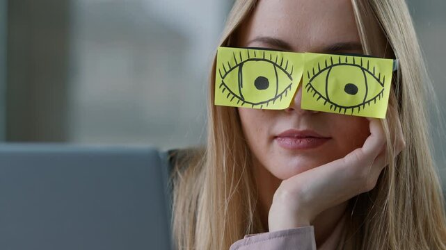 Close-up sleeping Caucasian business woman with drawing eyes sticky notes glasses sleep at workplace laptop computer boring job task businesswoman napping girl funny female suffering insomnia burnout