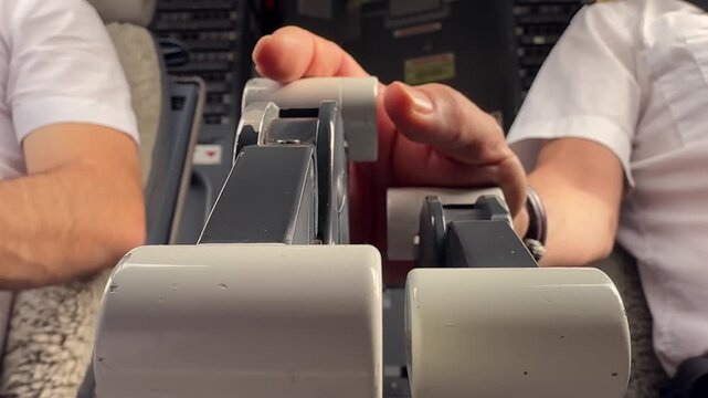 Extreme closeup view, low angle, of the hand of a pilot adjusting the engine throttle levers in a modern jet cockpit taxiing with only one engine to save fuel.