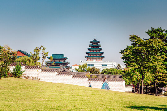 View of ancient Korean architecture rises majestically behind a traditional white wall, set against a vibrant green lawn under a clear sky, Seoul, Seoul, South Korea.