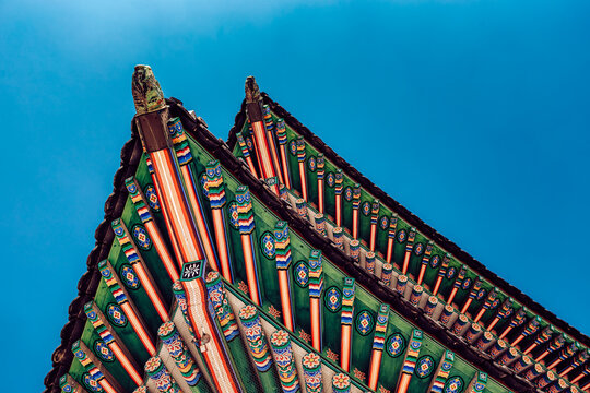 View of vibrant, ornate eaves adorned with intricate patterns reaching toward a brilliant blue sky, showcasing traditional Korean architecture, Seoul, Seoul, South Korea.