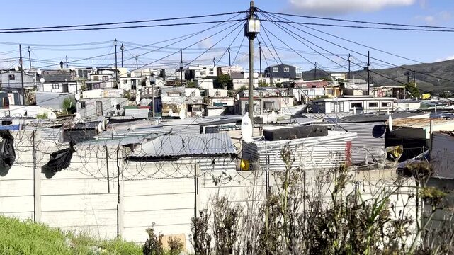 View over razor wire of squatter camp with tin shacks and power line connections