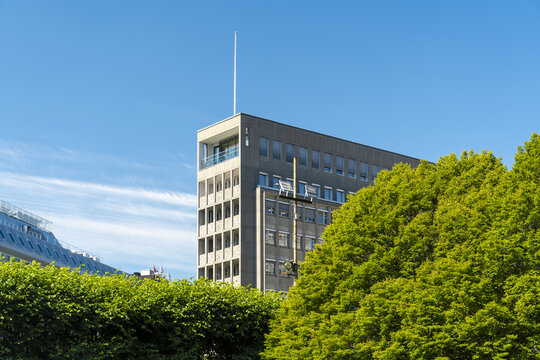 View of a modern, angular building with dark gray panels contrasted against bright green foliage under a clear blue sky, Oslo, Oslo, Norway.