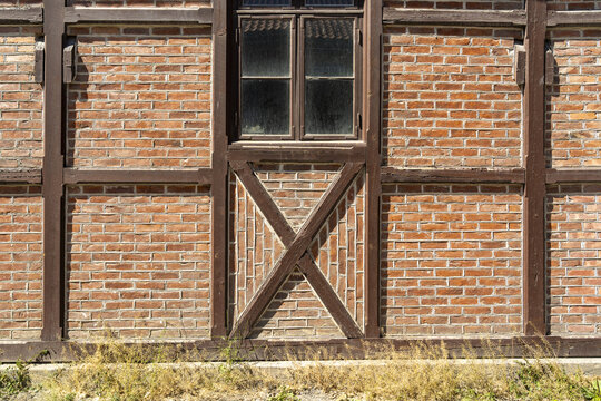 View of an old brick wall, accented by dark wooden beams and a small window, stands weathered yet charming against the bright daylight, Oslo, Oslo, Norway.